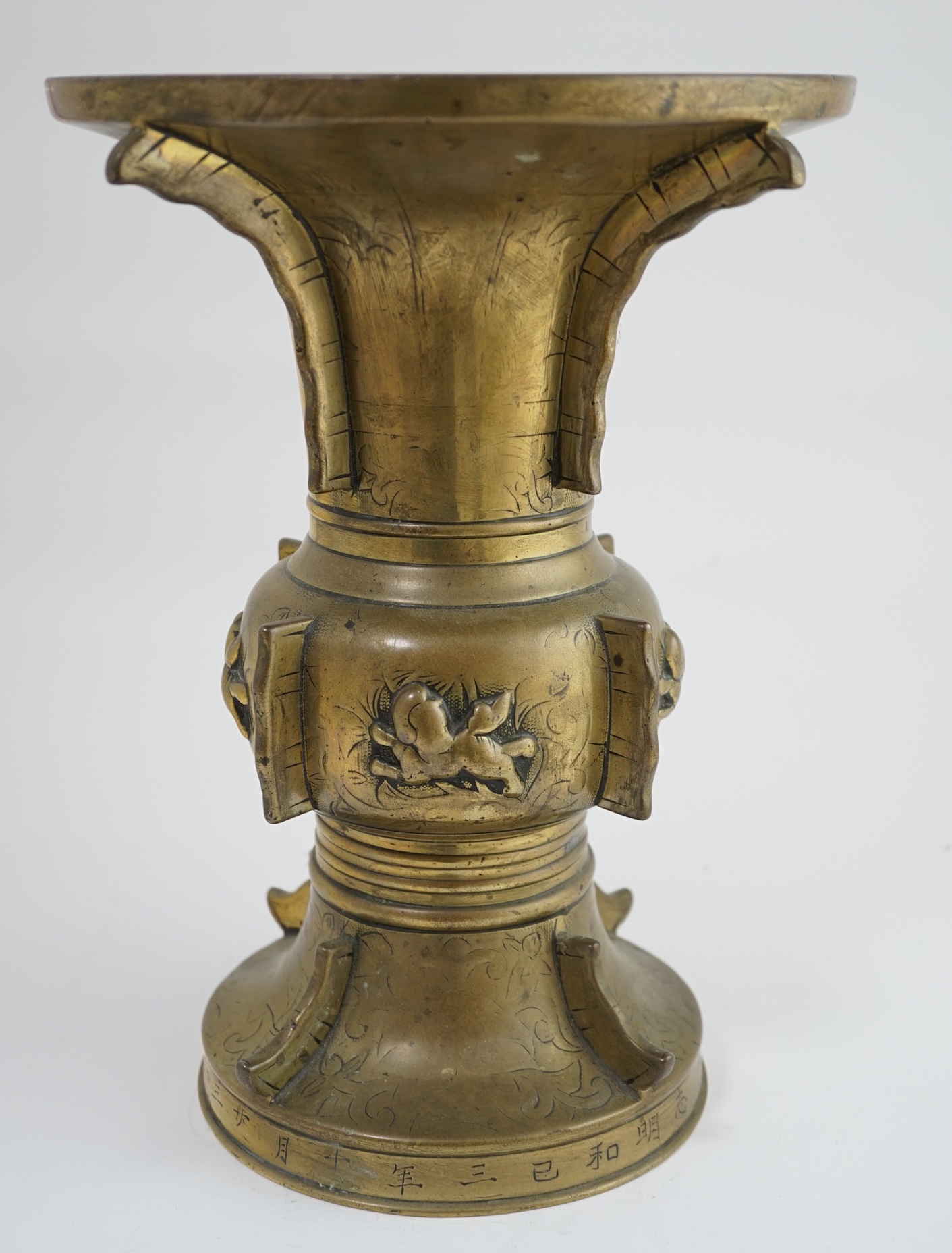 A Chinese inscribed archaistic bronze altar vase, gu, 19th century, the foliate engraved vase applied with raised fins and cast in relief with lion-dogs, the base engraved with an inscription, 33.7cm high. Condition - go